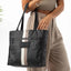 Person holding a black tote bag with a white stripe on a white background