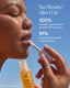 Person applying lip balm with Sea Results branding against a clear blue sky