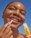 Woman applying Osea lip balm against a clear blue sky