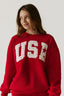 Woman wearing a red sweatshirt with 'USA' printed on it against a plain background