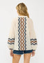 Person wearing a cream cardigan with zigzag pattern on sleeves and back, standing against a white background.