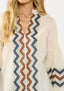 Person wearing a cream sweater with a zigzag patterned scarf
