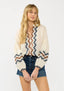 Woman wearing a cream blouse with a zigzag pattern and denim shorts on a white background
