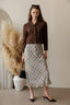 Woman wearing a brown jacket and plaid skirt standing in a room with decorative elements.