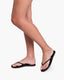 Black flip-flops worn on feet against a white background