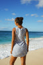 Woman in a sleeveless dress standing on a beach looking at the ocean.