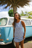 Woman in a blue floral dress standing next to a vintage blue and white van with palm trees in the background.