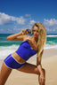 Woman in a blue swimsuit taking a selfie on a beach with ocean and sky in the background