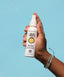 Hand holding a Sun Bum detangler spray bottle against a blue background