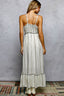 Woman wearing a long, light-colored dress with thin straps against a gray wall.