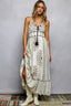 Woman wearing a long, embroidered dress with white boots against a plain background