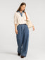 Woman wearing a cream blouse with blue denim accents and wide-leg jeans on a white background