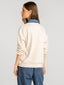 Woman wearing a cream sweater with a blue collar and blue jeans on a light gray background