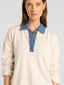 Woman wearing a beige long-sleeve shirt with a blue collar on a gray background