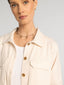 Woman wearing a beige jacket and white shirt with a necklace on a light gray background