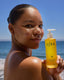 Woman holding a bottle of OSEA body oil on a beach