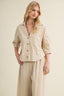 Woman wearing a beige button-up shirt and wide-leg pants against a plain background