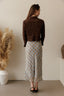 Woman wearing a brown jacket and checkered skirt standing against a plain wall with decorative elements.