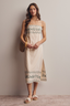 Woman wearing a beige dress with green patterns against a plain background