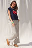 Woman wearing a navy sleeveless top with a red logo and striped pants against a white curtain background