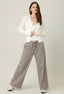 Woman wearing a white cardigan and striped pants on a plain background