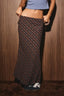 A person wearing a long dark plaid maxi skirt with a blue crop top, standing against a brown wood-paneled wall.