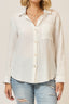 Woman wearing a white button-up shirt and ripped jeans against a plain background