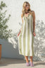 Woman wearing a green and white striped dress standing against a white wall with a plant in the background.