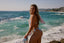 Woman in a bikini standing on a beach with ocean waves in the background