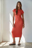 Woman wearing a red dress standing in a well-lit room with white curtains.