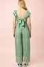 Green patterned jumpsuit with ruffled sleeves on a pink background
