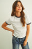 Woman wearing a white ribbed top with black trim and blue jeans on a plain background