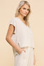 Woman wearing a light-colored sleeveless top and pleated skirt against a beige background