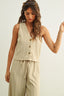 Woman wearing a beige sleeveless top and pants with sunglasses on her head against a plain background