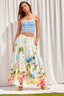 Woman wearing a blue checkered top and floral skirt against a white curtain background