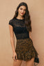 Woman wearing a black lace top and leopard print shorts against a beige background