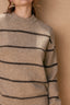 Close-up of a person wearing a beige sweater with black horizontal stripes against a beige background