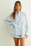 Woman wearing a light blue and white striped shirt and shorts on a plain background