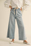 Person wearing light blue denim pants with a white shirt on a beige background