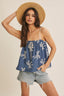 Woman wearing a blue top with white patterns and denim shorts, holding a straw hat.