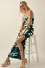Woman wearing a green and white patterned dress sitting on a stool against a plain background