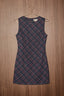 A sleeveless A-line dress with a small-scale plaid pattern in navy blue and burgundy, hanging on a metal hanger against a brown wood-paneled wall.