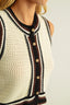 Close-up of a person wearing a crocheted cardigan with button details on a neutral background