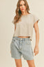 Woman wearing a beige top and denim shorts against a plain background