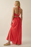 Woman wearing a red halter neck dress with cut-out back on a beige background
