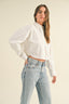 Woman wearing a white blouse and light blue jeans against a beige background