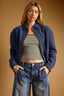 Woman wearing a navy jacket, striped top, and jeans against a beige background