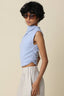 Woman wearing a light blue sleeveless top and beige pants against a beige background