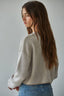 Woman wearing a beige knitted sweater and blue jeans against a plain background