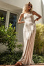 Woman in a long, light-colored dress standing outdoors with greenery around.